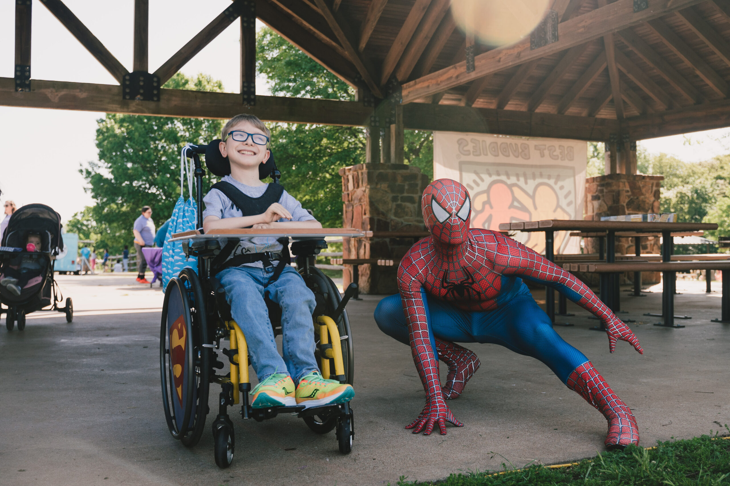 Smiling kid in wheelchair posing next to spider man in a park pavilion. Cultivate Event Planning