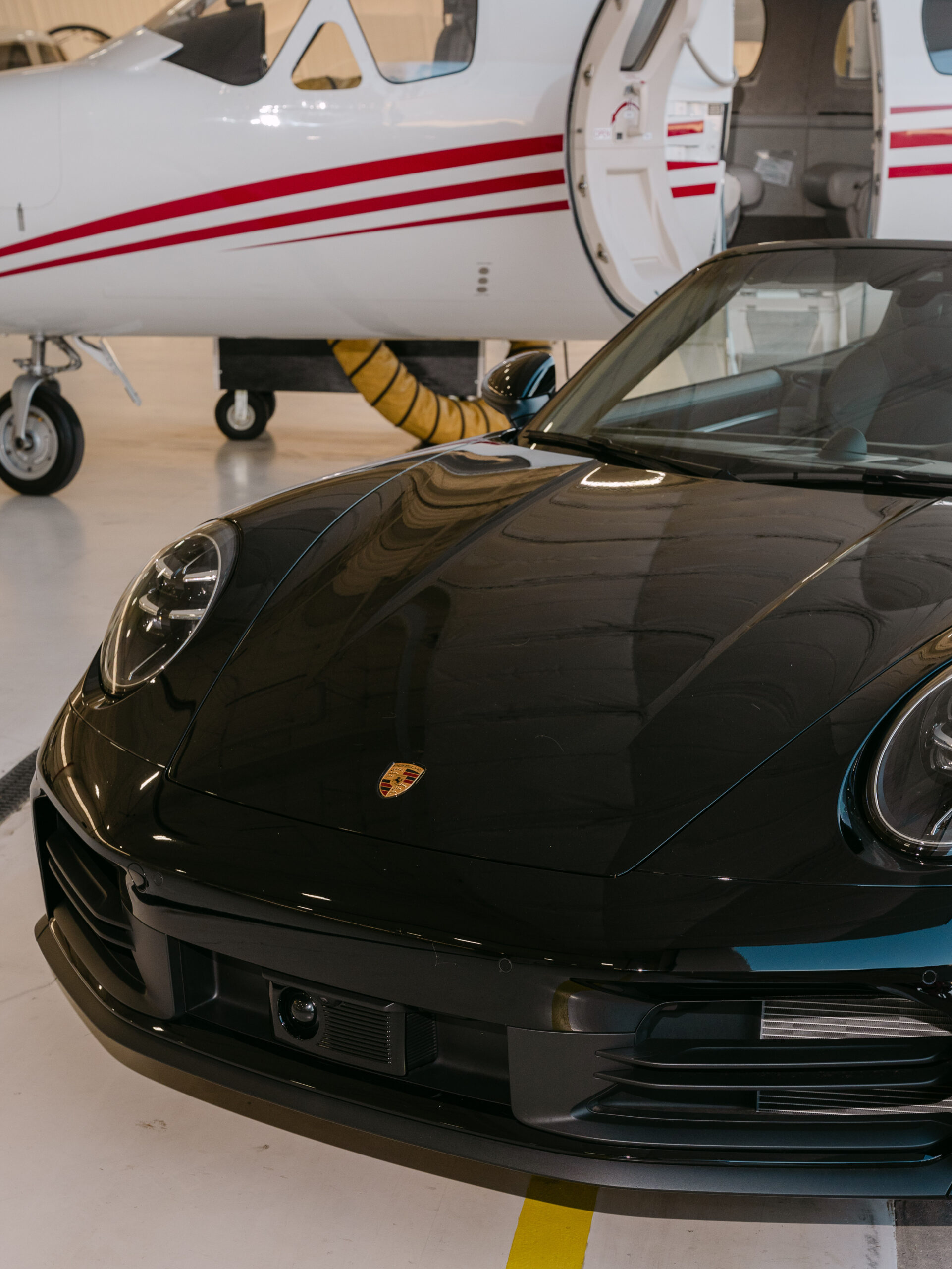 Black Porsche parked in front of a small plane parked in a hangar at a corporate event.