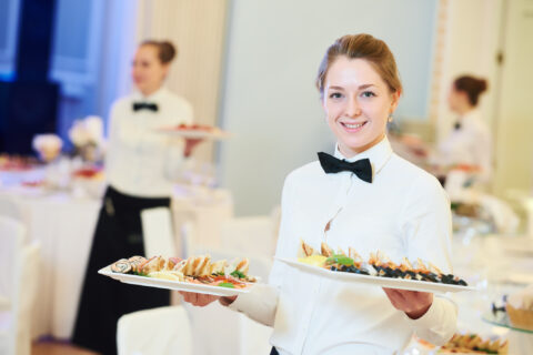 Young woman with food on dishes servicing in restaurant during catering the corporate event. Corporate event planning faqs - Cultivate Event Planning