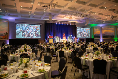 Corporate Christmas party set up in ballroom with screens, stage and tables ready for celebration by employees.